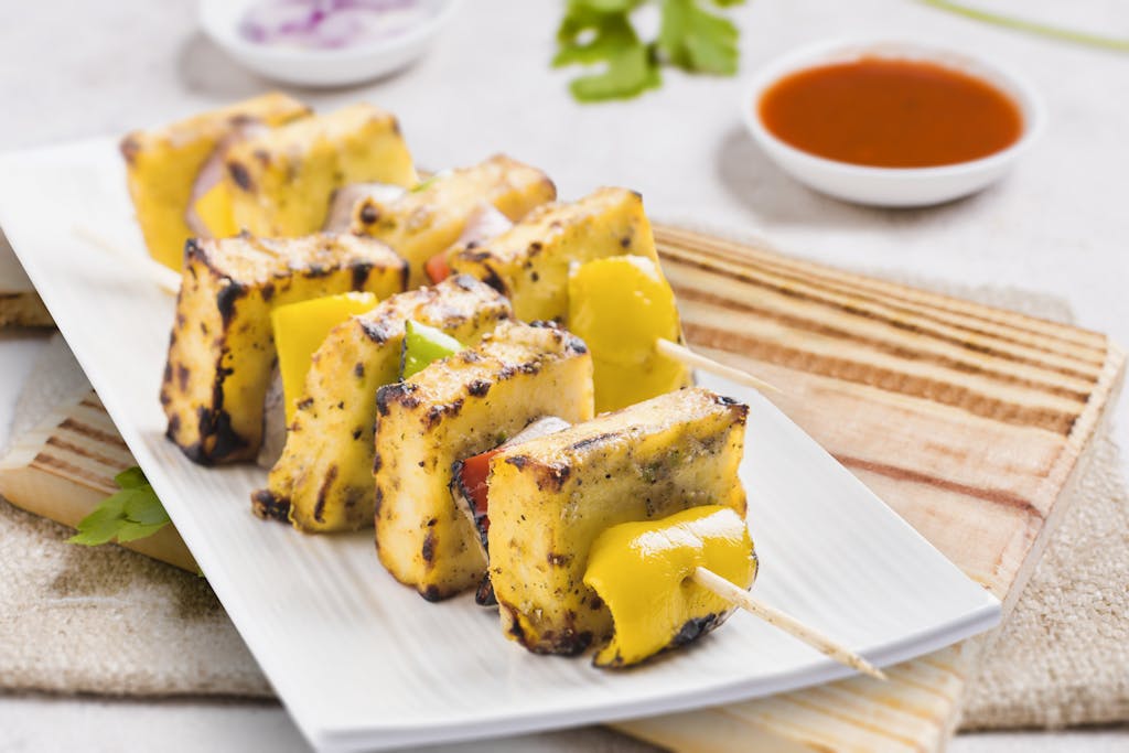 Tasty grilled paneer tikka skewers served on a plate with sauces, perfect for an Indian cuisine experience.